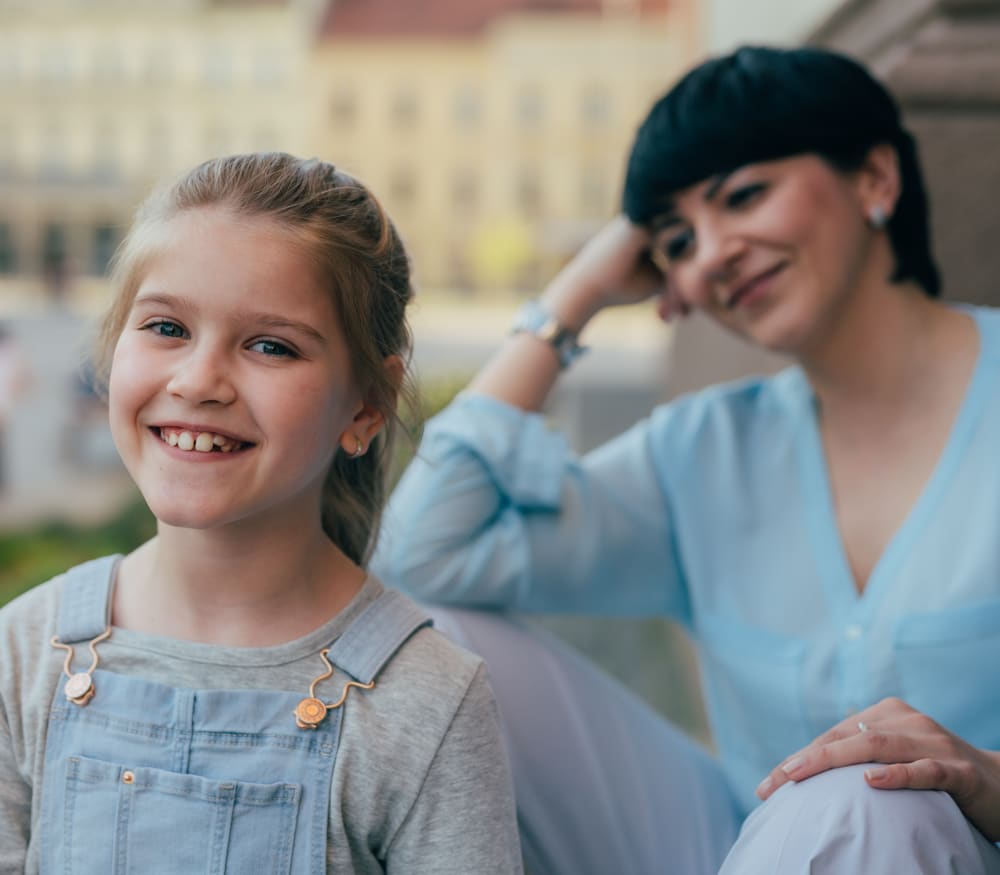 A mother sitting outside is admiring her daughter who is smiling.