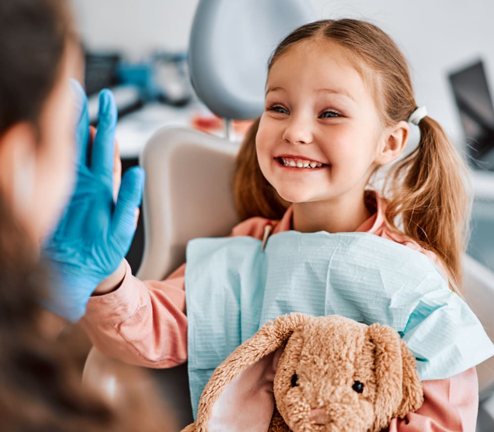 A little girl with two ponytails high-fives her dentist.