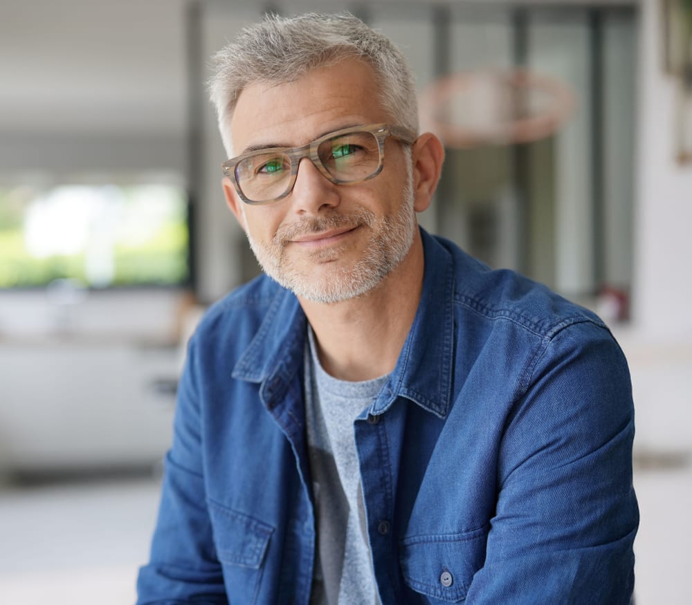 A man is with thick framed glasses is smiling at the camera.