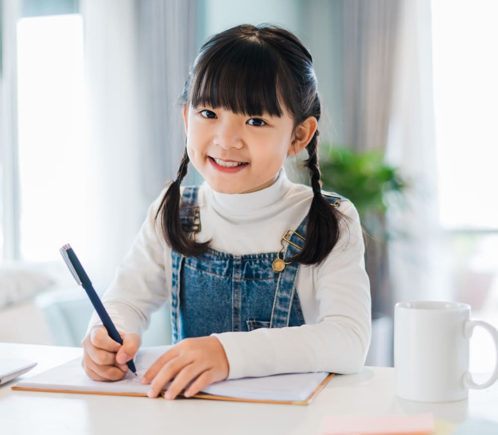 A young girl with pigtails is writing in a book.