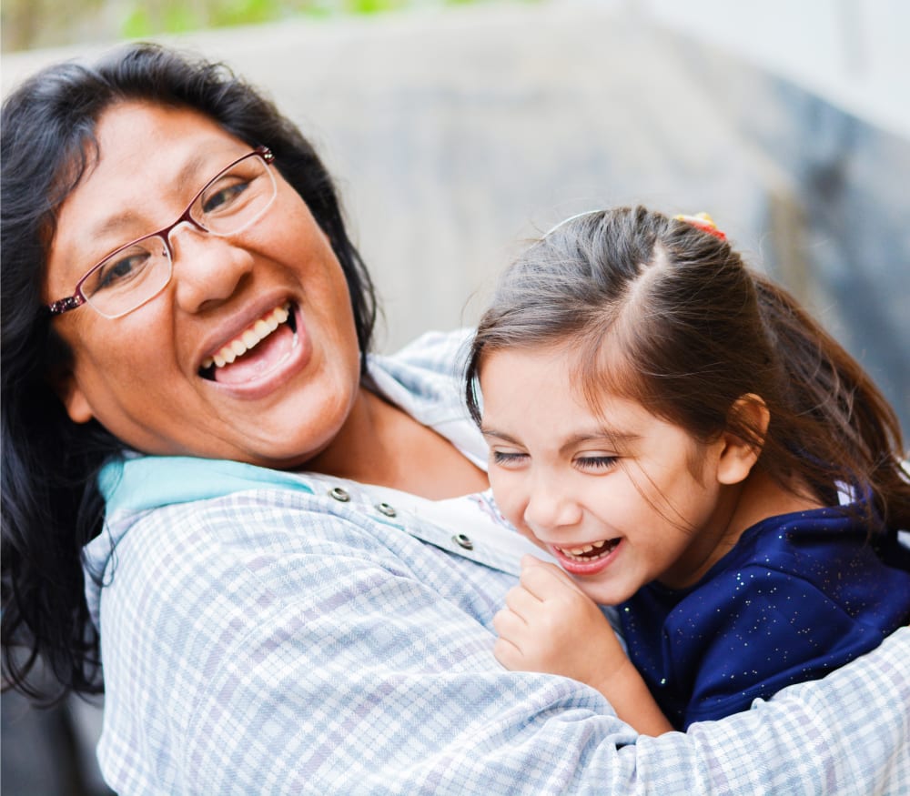 A woman is laughing and leaning back. In her arms is a young girl who is also laughing.