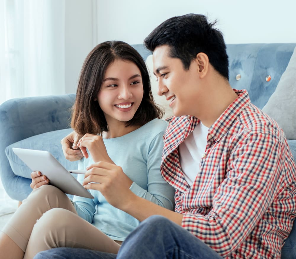A couple are sitting on the floor together against a couch looking at a tablet.